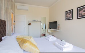 Une chambre d’hôtel avec un lit, une télévision, un miroir et deux tableaux représentant des motifs floraux, accrochés au mur.