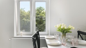 A dining area with a table set for four, a vase of white tulips, and a window with a view of trees. - Elite Apartments Sopot Seaside (Sopot)