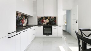 A modern kitchen with white cabinetry, a black countertop, and a floral backsplash. - Elite Apartments Sopot Seaside (Sopot)