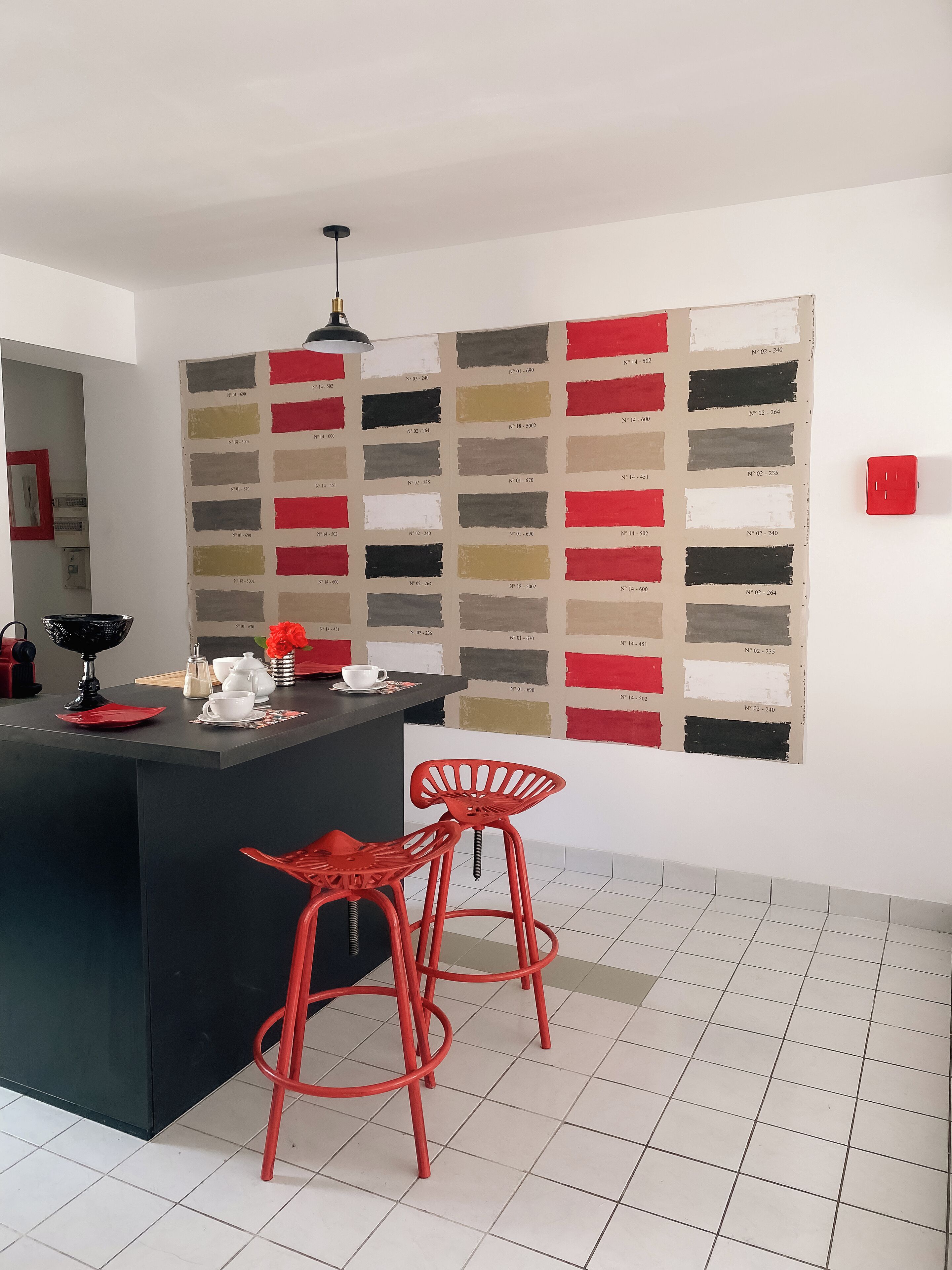 A modern kitchen with a central island, red bar stools, and a color palette wall.