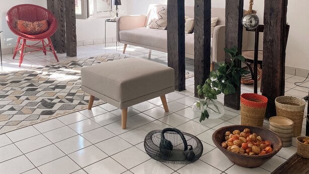 A modern living room with a tiled floor, a red chair, a beige sofa, and a wooden beam structure.