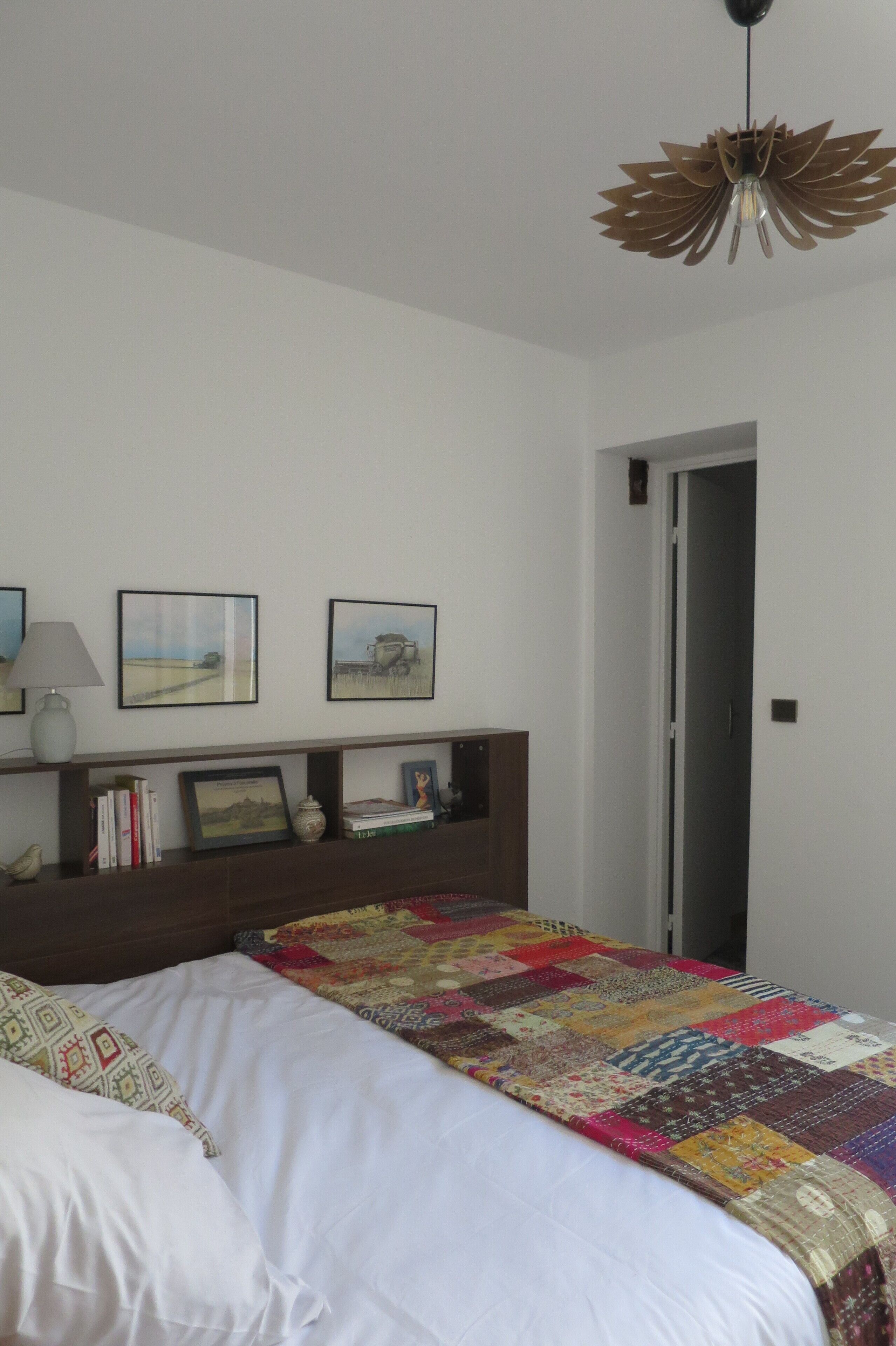 Une chambre à coucher avec un lit, une table de chevet, une lampe, des tableaux encadrés et une porte.