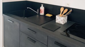A modern kitchen with a black countertop, a built-in sink, and a black backsplash. There is a shelf above the countertop holding a basket and glasses.