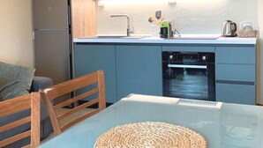 A compact kitchen with wooden cabinets, a built-in oven, and a dining area with a glass table and wooden chairs. - Villa Nice View in Pontagna (Temu)