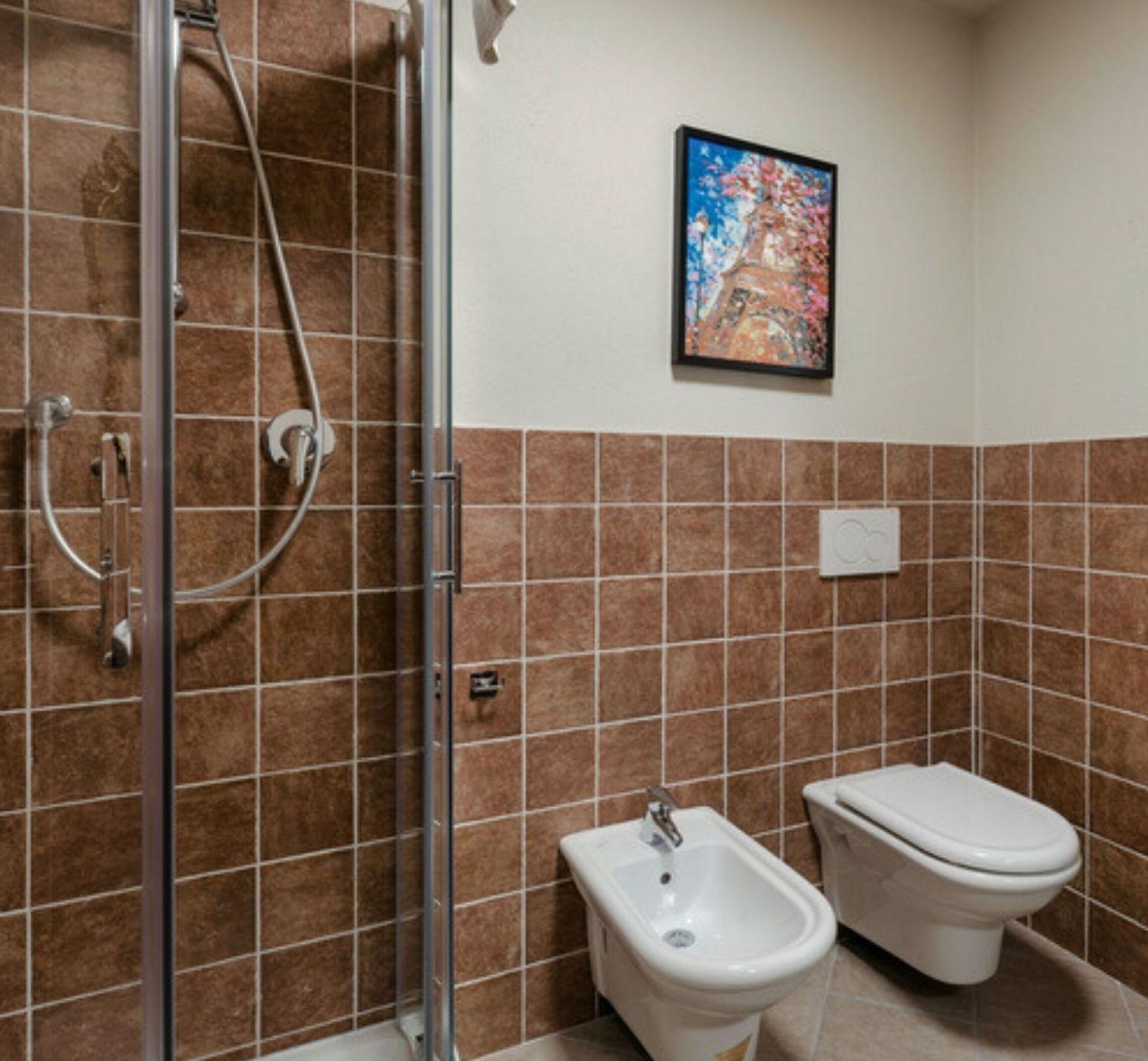Un baño con ducha, bidé e inodoro, con azulejos marrones y beiges.