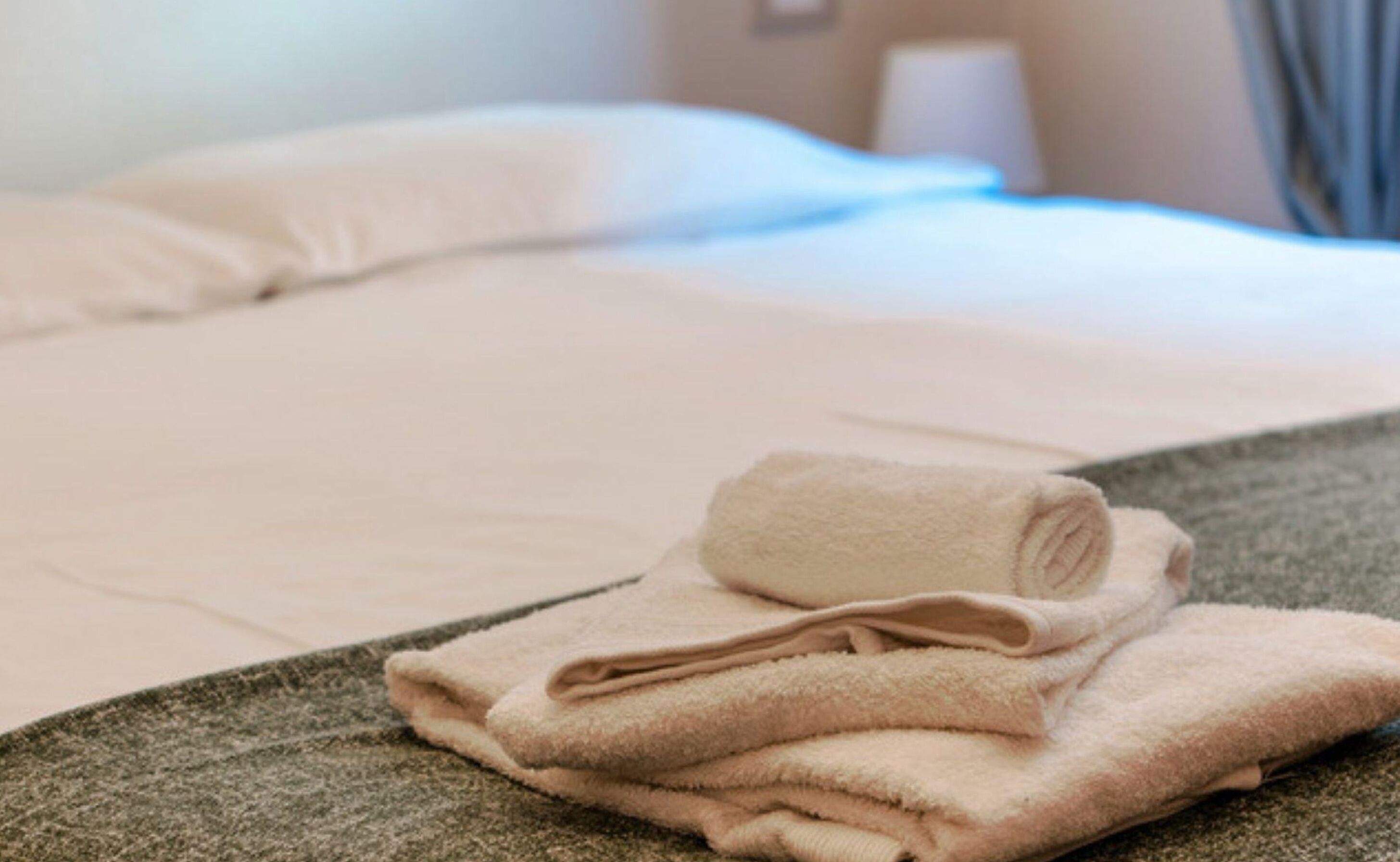A neatly made bed with white linens and a folded beige towel on a textured gray bedspread.
