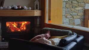 A cozy living room with a fireplace, a stone wall, and a view through a window. - Villa Nice View in Pontagna (Temu)