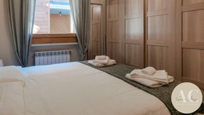 A bedroom with a bed, a radiator, a window with curtains, and wooden wardrobes. - Villa Nice View in Pontagna (Temu)
