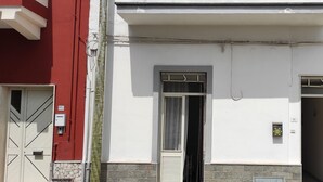 Un edificio blanco con una puerta roja, una ventana con reja metálica y un pequeño balcón con planta en maceta.