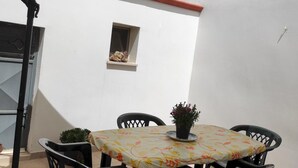 Un patio al aire libre con una mesa, sillas, un ventanal pequeño y una planta en maceta.
