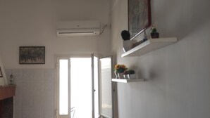 Un baño con una puerta blanca, un equipo de aire acondicionado, un estante con un florero y un cuadro en la pared.
