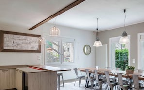 A modern kitchen with a wooden countertop, pendant lights, and a dining area with metal chairs and a wooden table. - La Tavolata in Incudine (Incudine)