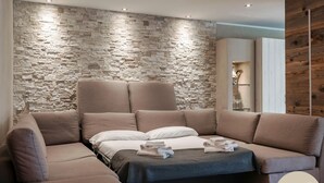 Ein modernes Wohnzimmer mit Steinwand, einem Ecksofa und einem Bett mit dunkler Tagesdecke.