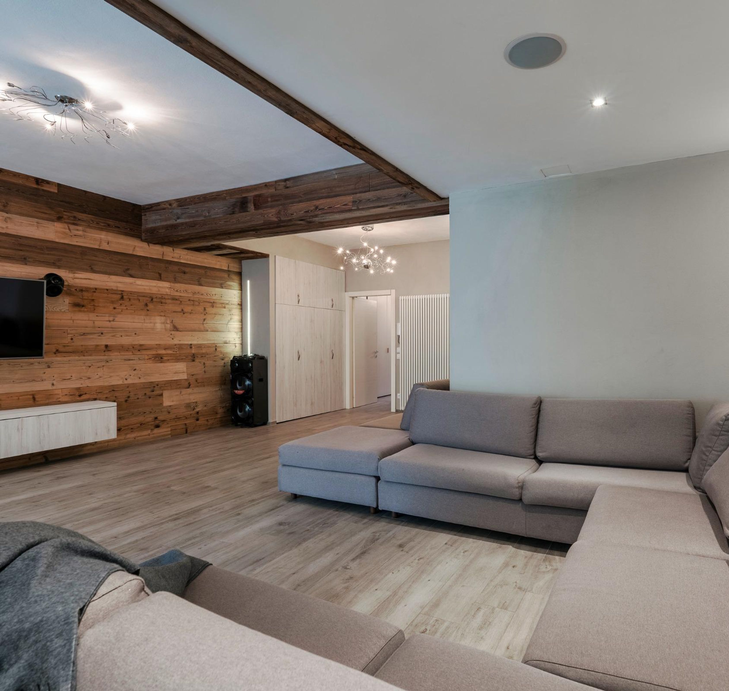 A modern living room with a sectional sofa, wooden walls, a flat-screen TV, and recessed lighting.
