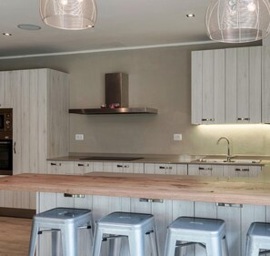 A modern kitchen with wooden cabinetry, a stainless steel range hood, a central island with stools, and pendant lighting.