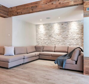 A modern living room with a stone wall, a wooden ceiling, and a fireplace.
