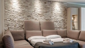 Un soggiorno moderno con parete in pietra, un divano componibile e un letto con coperta scura.