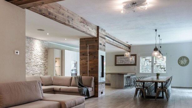 Ein modernes Wohnzimmer mit einem beigefarbenen Ecksofa, einem Holzesstisch mit Stühlen und einer Küche im Hintergrund.