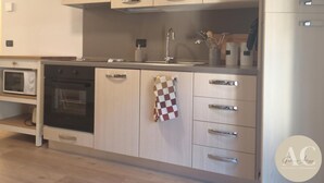 A modern kitchen with light wood cabinets, stainless steel appliances, and a checkered towel hanging on the door.