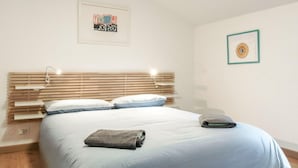 A bedroom with a wooden headboard, a bed with white bedding, a folded towel, and a framed artwork on the wall.