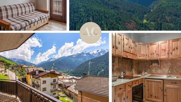 Ein gemütliches Zimmer mit einem Karo-Sofa, einer Holztür und einem Balkon mit Bergblick.