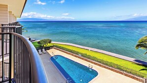 A swimming pool with a view of the ocean, a grassy area, and a railing. - Beachfront bliss near the Heart of Kaanapali shopping (Lahaina)