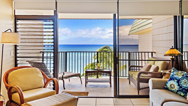 A balcony with a view of the ocean, furnished with wicker chairs and a sofa, and a table with a lamp. - Beachfront bliss near the Heart of Kaanapali shopping (Lahaina)