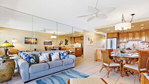 A spacious living room with a sofa, a dining area with a table and chairs, and a kitchen with wooden cabinets. - Beachfront bliss near the Heart of Kaanapali shopping (Lahaina)