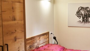 Ein Schlafzimmer mit einem hölzernen Kopfende, einer rosa Tagesdecke, einer Wandlampe und einem Bärenbild.
