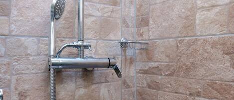 A shower with a handheld showerhead and a wall-mounted faucet against a stone wall.