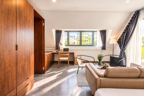 A modern room with a wooden wardrobe, a desk with a laptop, a sofa, and a view of buildings through the window. - Nexus House Thao Dien (Ho Chi Minh City)