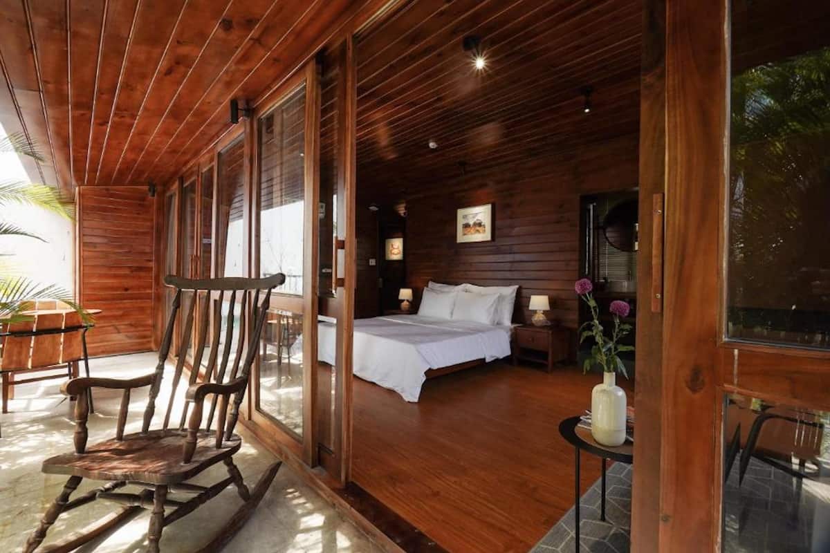 A wooden cabin with a large bed, a rocking chair, and a small table with a vase.