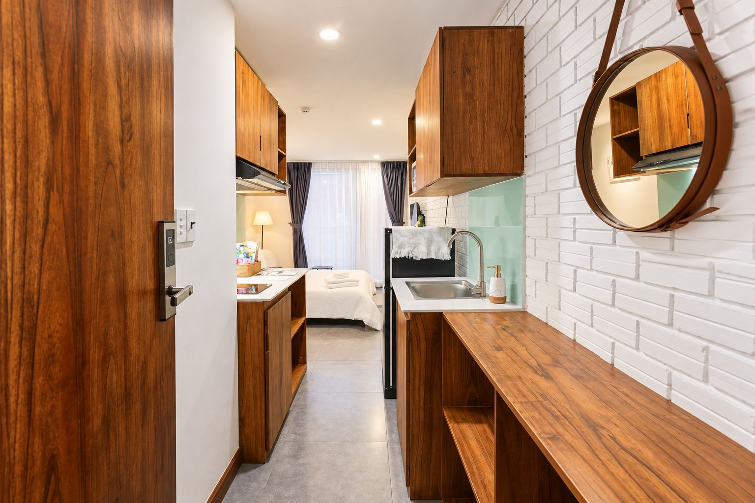 A compact kitchenette with wooden cabinets, a sink, and a round mirror on the wall.