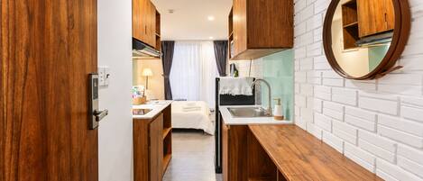 A compact kitchenette with wooden cabinets, a sink, and a round mirror on the wall.