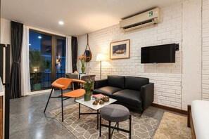 A modern living room with a black leather sofa, a round coffee table, and an orange chair. There is a flat-screen TV mounted on the wall and a potted plant on the table. - Nexus House Thao Dien (Ho Chi Minh City)