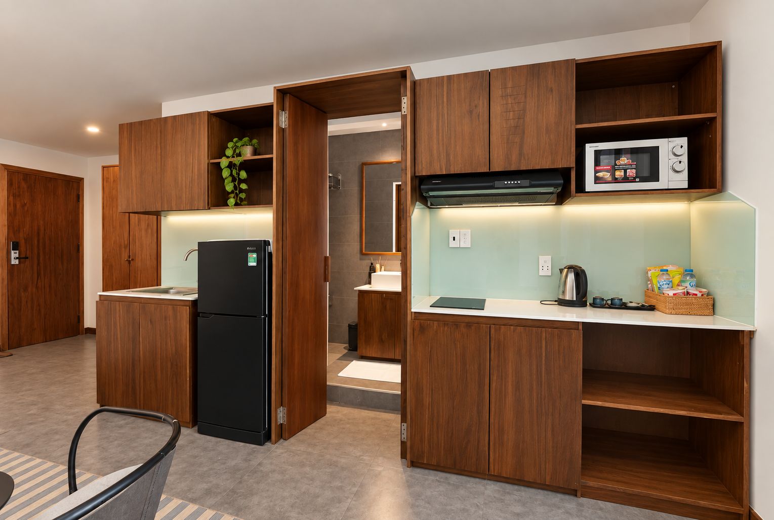 A modern kitchen with wooden cabinetry, a black refrigerator, a microwave, and a kettle.