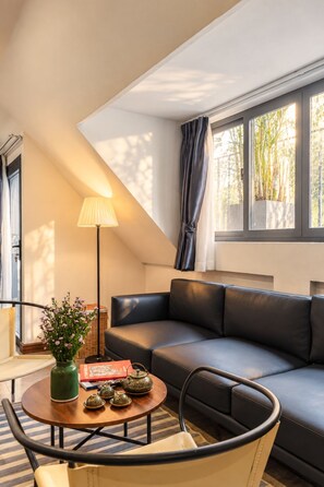 A modern living room with a sofa, a round coffee table with decorative items, a floor lamp, and a view of greenery through a window. - Nexus House Thao Dien (Ho Chi Minh City)