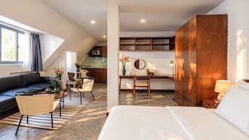 Una habitación de hotel moderna con una cama grande, un sofá, una zona de comedor y una cocina al fondo.