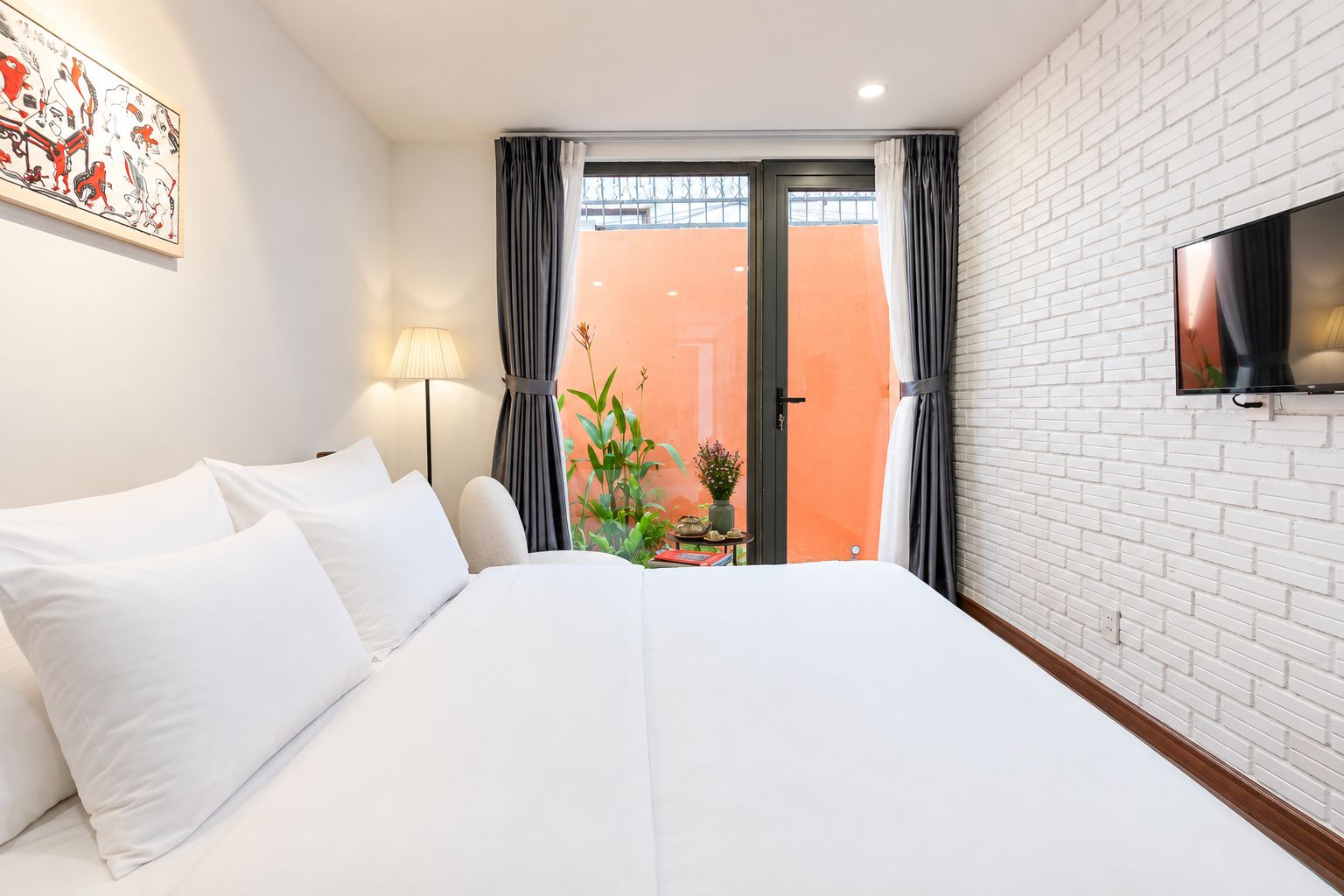 A hotel room with a bed, a TV mounted on the wall, a window with curtains, and a view of the outside.