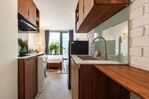A compact kitchen with wooden cabinets, a built-in washing machine, and a large window. - Nexus House Thao Dien (Ho Chi Minh City)