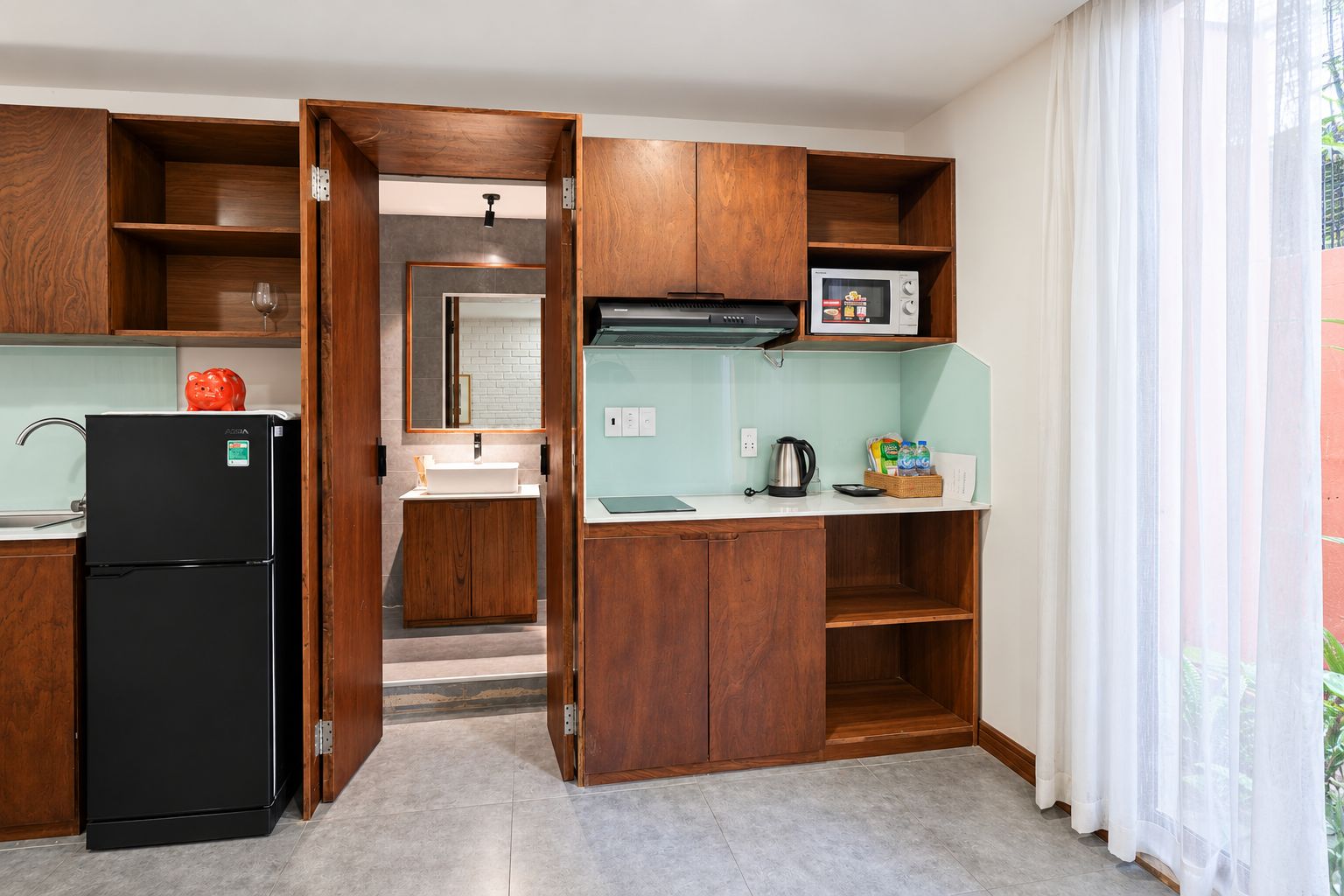 A compact kitchen with wooden cabinets, a black refrigerator, a microwave, and a kettle.