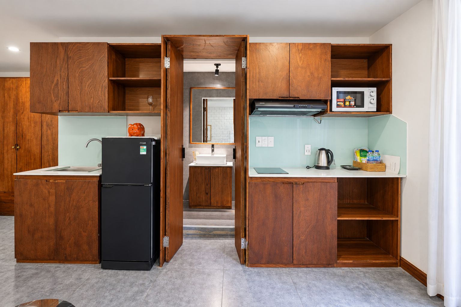 A compact kitchen with wooden cabinetry, a black refrigerator, and a microwave on the countertop.