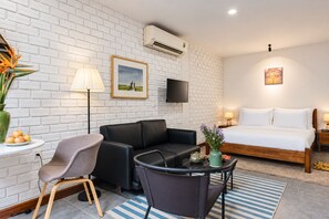 A hotel room with a bed, a sofa, a chair, a small table with a vase, and a flat-screen TV mounted on the wall. - Nexus House Thao Dien (Ho Chi Minh City)