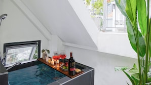 Ein modernes Badezimmer mit integriertem Whirlpool, einem Fenster mit Blick auf die Stadt und einer großen, grünen Pflanze.