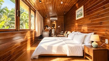 A wooden cabin bedroom with a large bed, a nightstand, a lamp, and a bathroom with a sink and shower.
