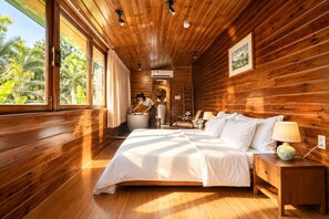 Un dormitorio de cabaña de madera con una cama grande, una mesita de noche, una lámpara y un baño con lavamanos y ducha.