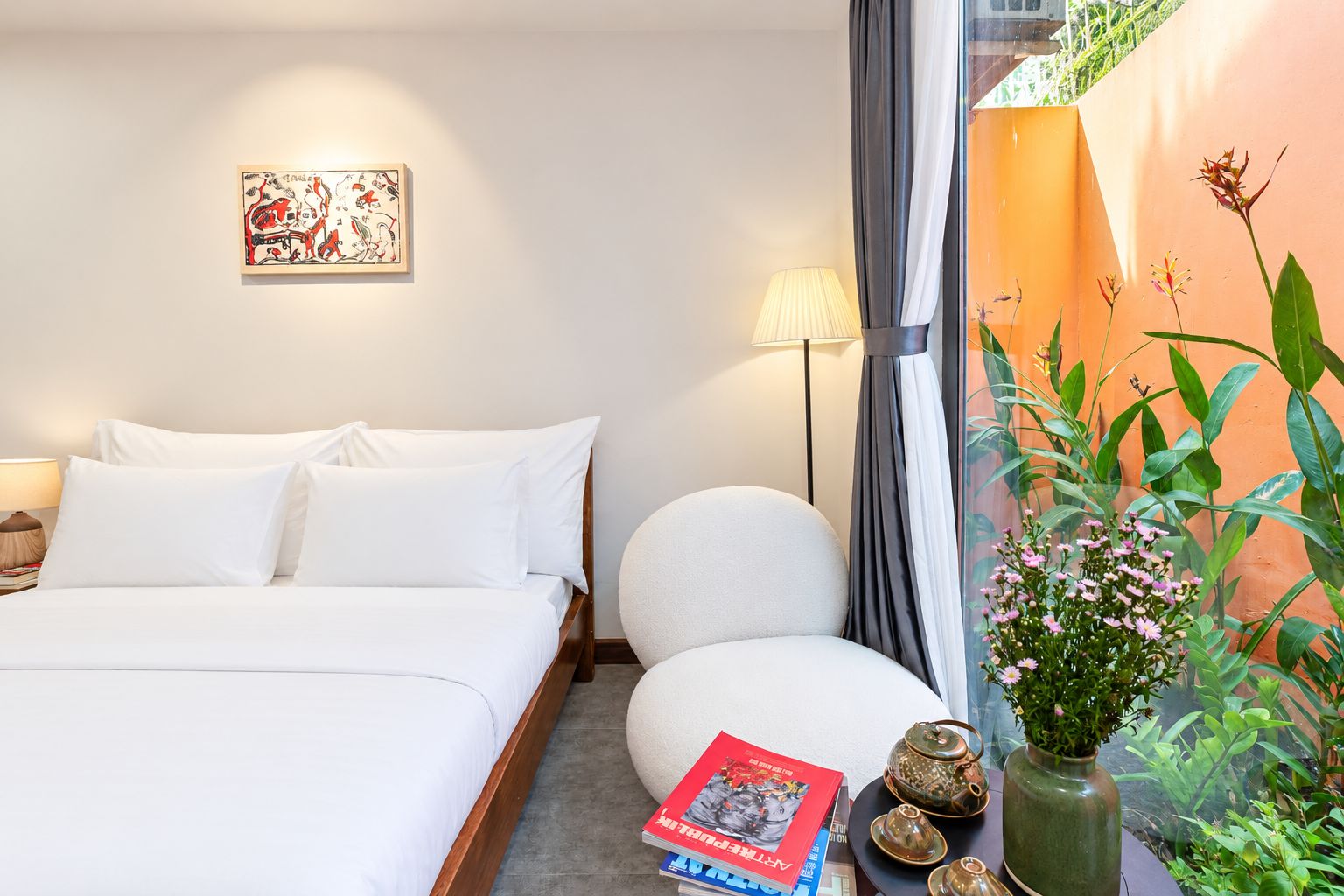 A hotel room with a bed, bedside table, lamp, and a wall-mounted artwork.