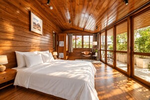 Un dormitorio con techo de madera, una cama grande, una mesita de noche, una silla y una ventana con vista a follaje.