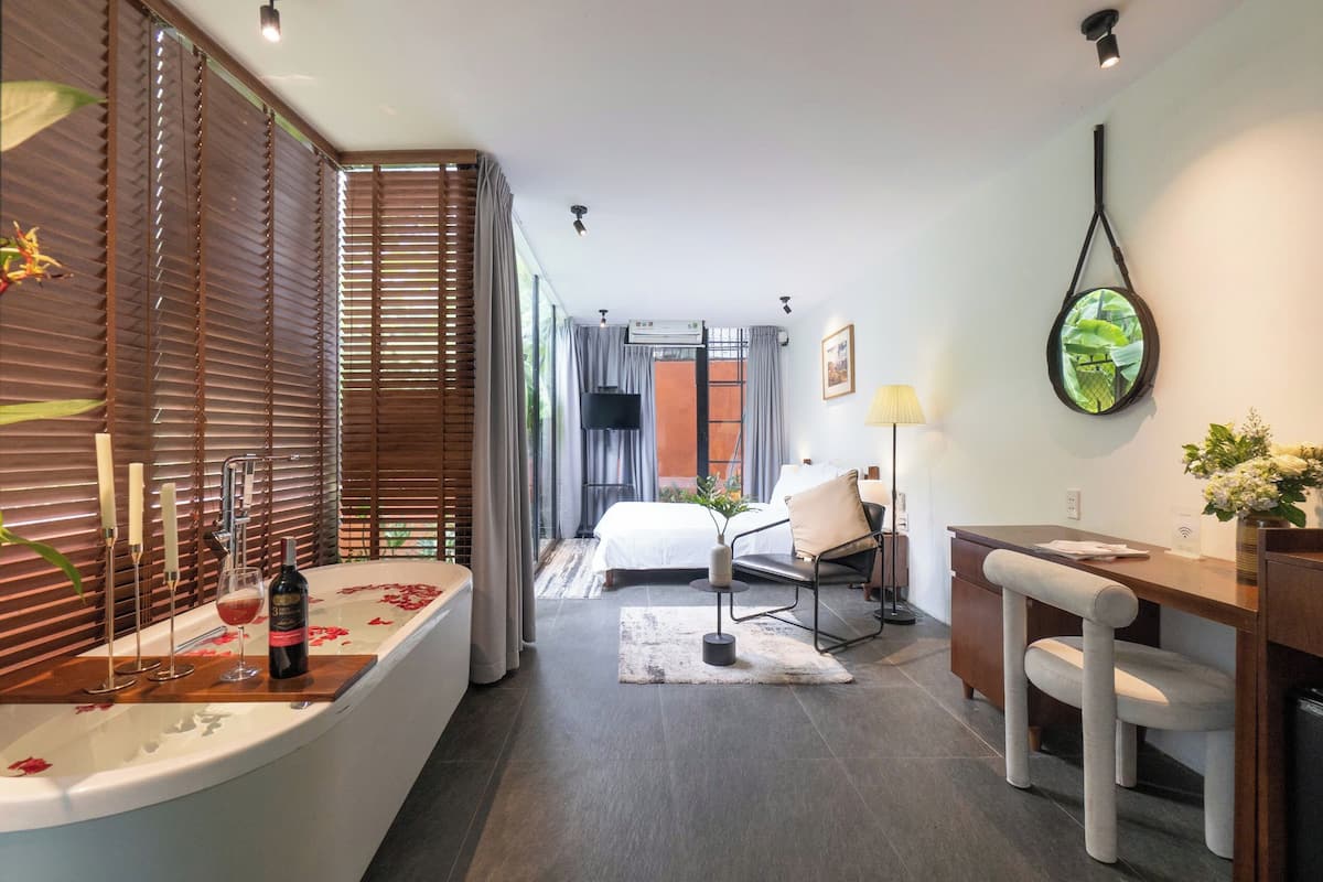 A modern hotel room with a bathtub, a desk, a chair, and a bed.