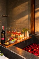 Un espacio de spa con un banco de madera, velas, una botella de vino, copas y un bol de fruta.